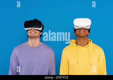 hipster interrazziali in cuffie per realtà virtuale isolate su blu Foto Stock