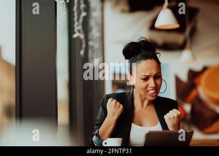 una donna si siede in un caffè con le braccia sollevate E celebrando un concetto di lavoro ben fatto.Business Foto Stock