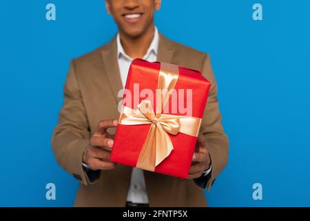 vista ritagliata delle armi di giovane african american mans che presentano il regalo scatola isolata in blu Foto Stock