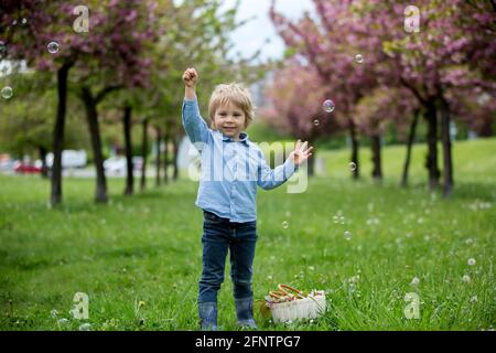 Bambino biondo, ragazzo carino in abbigliamento casual, giocando con bolle di sapone nel parco, correre felicemente Foto Stock