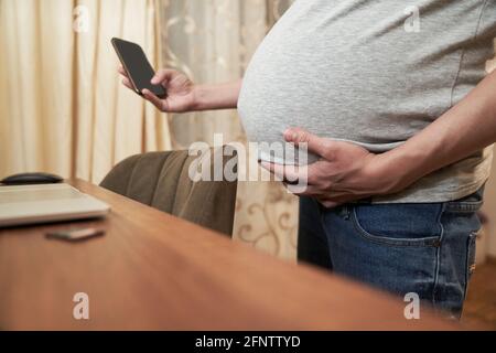 Donna incinta a casa con il telefono si trova vicino a un tavolo con il computer, concetto: Shopping online. Foto di alta qualità Foto Stock