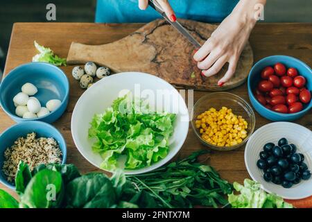 Donna taglia le verdure per insalata su un tagliere. Cucinare a casa. Foto Stock