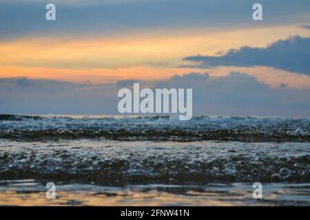 primo piano di onde di acqua di mare con bolle. Acqua di mare blu al tramonto. Foto Stock
