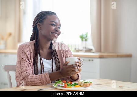 Mattina relax. Happy African Woman bere caffè mentre si ha la prima colazione in cucina Foto Stock