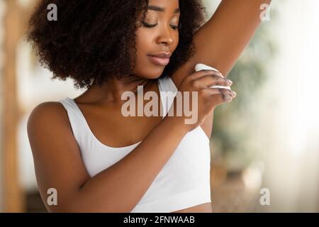 Bellissima donna nera che usa l'epilatore per rimuovere i peli superflui la sua ascella a casa Foto Stock