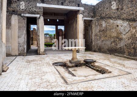 Atrio quadrato che ha un impianto centrale (serbatoio dell'acqua). Il pavimento dell'atrio è costituito da lava frantumata decorata con piccoli trucioli di marmo bianco. Casa del frutteto - Sito archeologico di Pompei, Italia Foto Stock