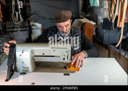 Anziano vecchio hipster sopportato uomo con cappellotto piatto che lavora con pelle e macchina da cucire Foto Stock