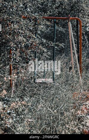 Un'oscillazione sopravfatta e abbandonata regolata nel mezzo della foresta. Un sacco di erba. La natura assume il controllo. Sensazioni strane. Foto Stock