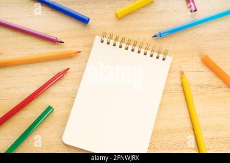 Notebook vuoto circondato da pennarelli colorati su un tavolo di legno. Bock up. Vista dall'alto Foto Stock