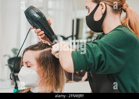 Lo stylist usa un asciugacapelli per modellare i capelli dopo la colorazione. Nuovo Foto Stock