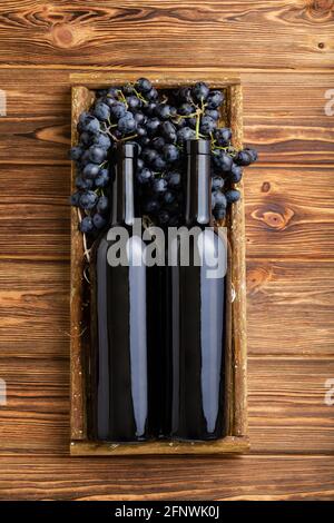 Composizione di due bottiglie di vino rosso su tavola di legno marrone. Bottiglie di vino rosso in scatola su uve nere mature su tavola di legno. Etichetta del vino della vecchia collezione Foto Stock