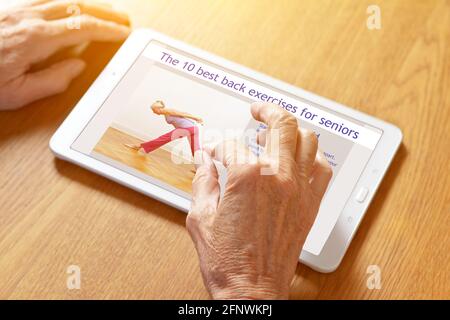 Concetto domestico di idoneità: Mani di una donna anziana che ingrandisce sulle istruzioni per gli esercizi posteriori su un pc del tablet. Foto Stock