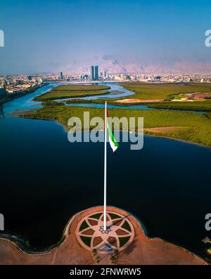 Bandiera nazionale degli Emirati Arabi Uniti e Ras al Khaimah emirano Il punto di riferimento e lo skyline aereo degli Emirati Arabi Uniti del nord vista sopra le mangrovie an Foto Stock