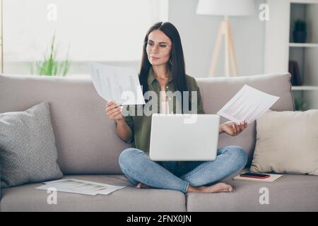 Ritratto di bella ragazza sicura e intelligente messa a fuoco seduta sul divano utilizzo di un computer portatile per l'analisi della lettura di documenti in casa, in ambienti interni piani Foto Stock