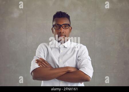 Studio ritratto di serio uomo nero in camicia bianca e. occhiali in piedi braccia ripiegate Foto Stock