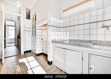 Retrò casa di design interno di cucina con pareti piastrellate e. pavimento arredato con mobili bianchi e banco in marmo in vecchio appartamento alla moda Foto Stock