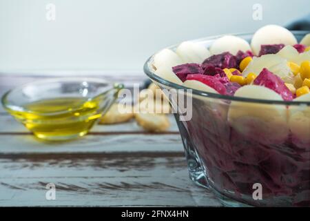 Barbabietola, ananas, mais, cuori di palma e insalata di cicoria con olio d'oliva e basilico in una ciotola di vetro su un tavolo rustico in stile still life. Verdure sane Foto Stock