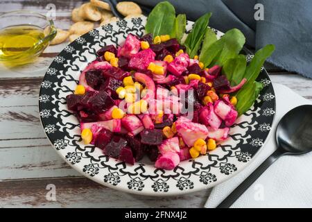 Insalata di barbabietole, ananas, mais e cicoria con olio d'oliva e basilico su un piatto su un tavolo rustico in stile still life. Concetto di verdure sane. Foto Stock