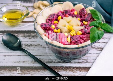 Barbabietola, ananas, mais, cuori di palma e insalata di cicoria con olio d'oliva e basilico in una ciotola di vetro su un tavolo rustico in stile still life. Verdure sane Foto Stock