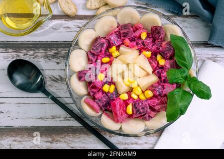 Barbabietola, ananas, mais, cuori di palma e insalata di cicoria con olio d'oliva e basilico in una ciotola di vetro su un tavolo rustico in stile still life. Verdure sane Foto Stock