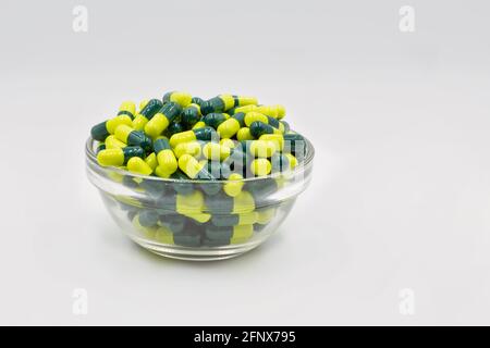 Capsule mediche di colore giallo verde in una ciotola di vetro con un'ostruzione di colore bianco sfondo Foto Stock