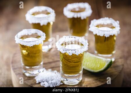 Diversi bicchieri di Tequila messicana Gold con limone e sale su tavolo di legno Foto Stock