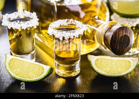 Diversi bicchieri di Tequila messicana Gold con limone e sale su tavolo di legno Foto Stock