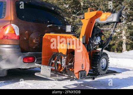 Primo piano di un aratro da neve meccanico arancione luminoso parcheggiato in un vialetto, pochi istanti prima di essere utilizzato per rimuovere la neve fresca da una casa di campagna. Foto Stock