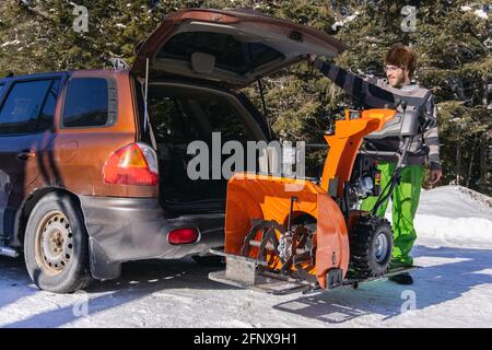 Grandangolare di un aratro meccanico arancione brillante che viene scaricato dal bagagliaio di un'auto e pronto per essere utilizzato per la rimozione della neve fresca. Foto Stock