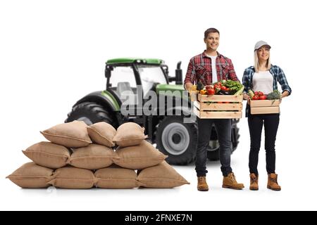 Giovani agricoltori che trasportano casse con verdure e posare davanti di un trattore isolato su sfondo bianco Foto Stock