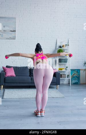 vista posteriore di giovane donna in leggings allenamento con manubri a casa Foto Stock