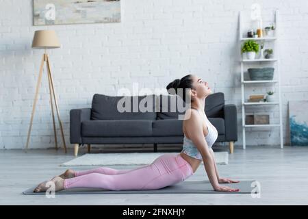 vista laterale della giovane donna bruna che pratica yoga in alto posa cobra Foto Stock