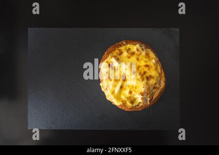 vista dall'alto del pane rotondo e croccante cotto farcito con formaggio alla griglia su un piatto d'ardesia con fondo nero. Fotografia alimentare Foto Stock