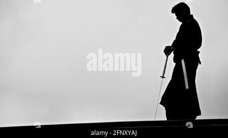 Silhouette di un samurai in un ambiente urbano con una katana in una scabbard bianca. Foto Stock