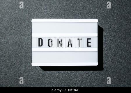 Lavagna luminosa su sfondo nero con le parole DONATE in lettere nere. Denaro Foto Stock