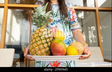 Femmina in un vestito colorato che tiene un piatto grande di frutti tropicali Foto Stock