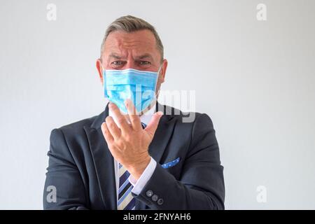 Uomo d'affari tormentato in vestito e maschera di faccia cercando di spiegare il suo punto di vista gesturing con la sua mano con un espressione angosciata sconvolguta sul bianco Foto Stock