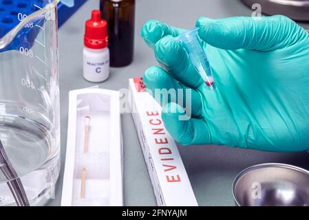 Lo scienziato della polizia tiene una fiala con una traccia di sangue sul tampone per indagare l'omicidio nel laboratorio di criminalità, immagine concettuale Foto Stock