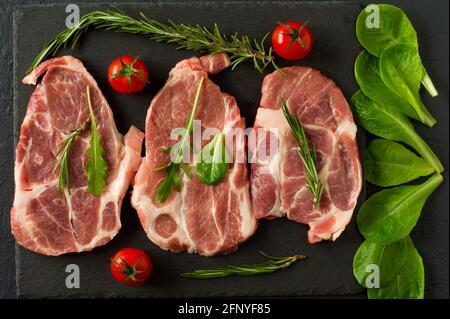 Cibo biologico fresco di maiale grezzo collo su ardesia nera con rosmarino, cipolla e pomodori Foto Stock