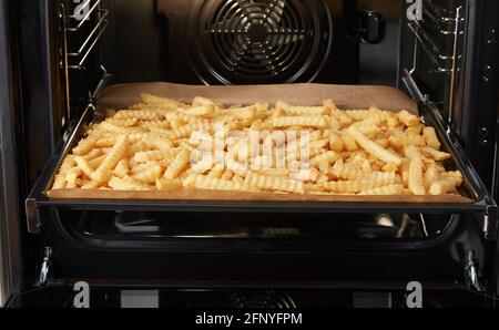 Vassoio con un mazzo di patatine fritte tagliate a papera forno durante la preparazione del pranzo in cucina contemporanea Foto Stock