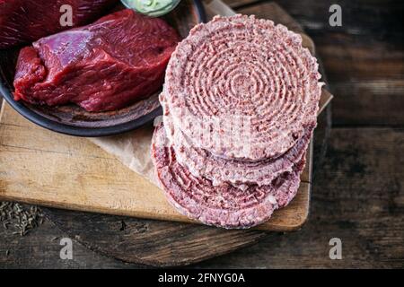 Semilavorati e carne su fondo di legno. Tagli di carne surgelati. Prodotto a base di carne di maiale, manzo. Cotoletta di hamburger rotonda piatta. Foto Stock