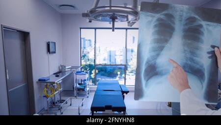 Sezione centrale del medico che esamina il rapporto a raggi X contro la sala operatoria in background Foto Stock