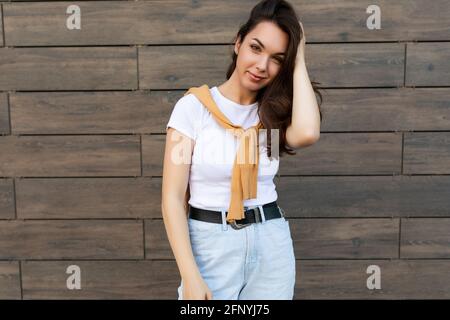 Ritratto di giovane bella donna bruna felice positiva in piedi contro parete marrone in strada e vestito elegante Foto Stock