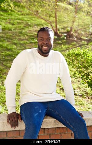 Giovane afroamericano sorridente seduto su un muro. Felice uomo latino. Foto di alta qualità Foto Stock