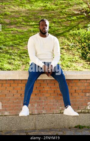 Giovane afroamericano seduto su un muro. Uomo latino che cammina per la città. Foto di alta qualità Foto Stock