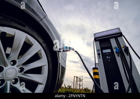 Auto EV collegata al caricabatteria e alla stazione di ricarica EV. Stazione di ricarica per auto elettrica vicino all'autostrada. Auto elettrica. Ricarica dell'auto a emissioni zero. Privo di carbonio Foto Stock