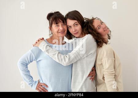 Allegra madre adulta abbracciando affascinanti giovani figlie mentre si sta in piedi sfondo bianco in studio e guardando la fotocamera Foto Stock