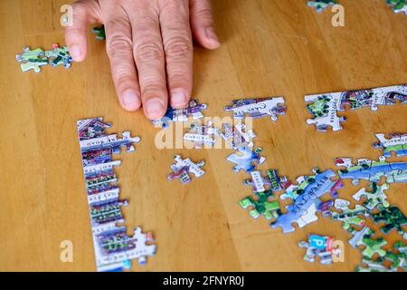 Primo piano su primo piano di mano sul pezzo puzzle jigsaw completamento Pezzi ad un bordo d'angolo su un tavolo di legno UK KATHY DEWITT Foto Stock