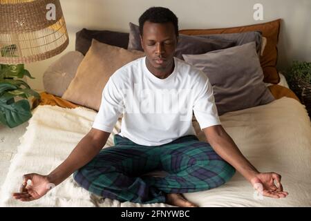 Giovane africano meditando seduto in camera in mattina Foto Stock