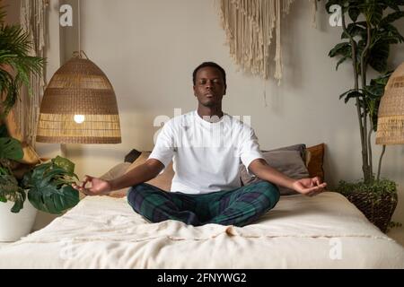 Giovane africano meditando seduto in camera in mattina Foto Stock
